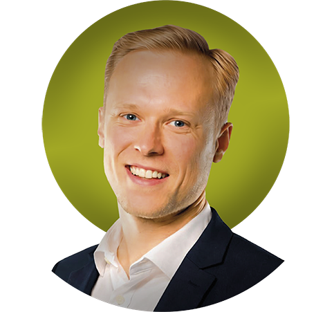 Henkilö pukeutuneena valkoiseen kauluspaitaan ja tummansiniseen pukuun seisoo neutraalin valkoista taustaa vasten. Henkilön hiukset ovat siististi kammatut ja hänet on rajattu rintakehästä ylöspäin.