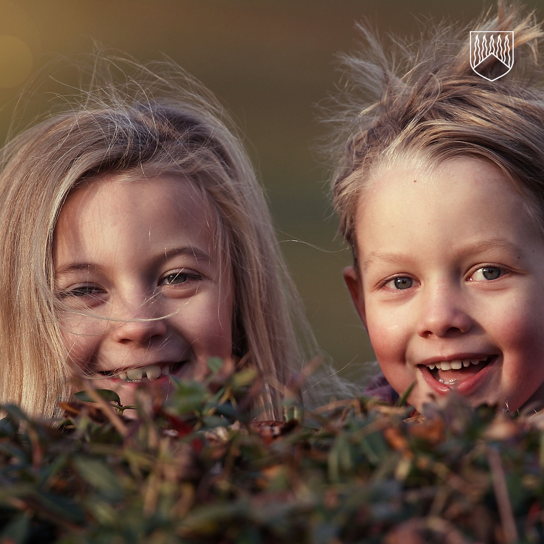 Kaksi lasta kurkkimassa varpumättään takaa.